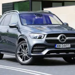 Szary Mercedes GLE 300 d stoi przed nowoczesnym budynkiem. Elegancki SUV z charakterystycznym grillem i felgami.