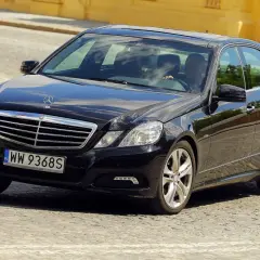 Elegancki, czarny Mercedes-Benz Klasa E porusza się po brukowanej ulicy.