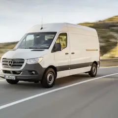 Biały Mercedes-Benz Sprinter z silnikiem diesla pędzi po krętej drodze, mijając wzgórza.