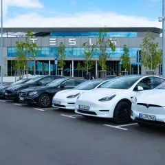 Rząd białych i czarnych Tesli zaparkowany przed budynkiem z napisem "TESLA". Czy to Tesla z jakiego kraju?