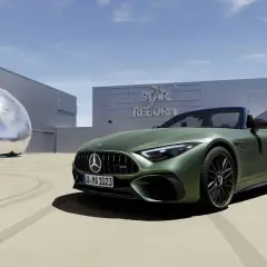 Zielony Mercedes SL 63 AMG na tle budynku z napisem "The Star is Reborn" i futurystyczną rzeźbą.