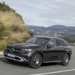 Czarny Mercedes GLC 200 4MATIC pokonuje zakręt na górskiej drodze, otoczony zielonymi wzgórzami i skalistymi zboczami.